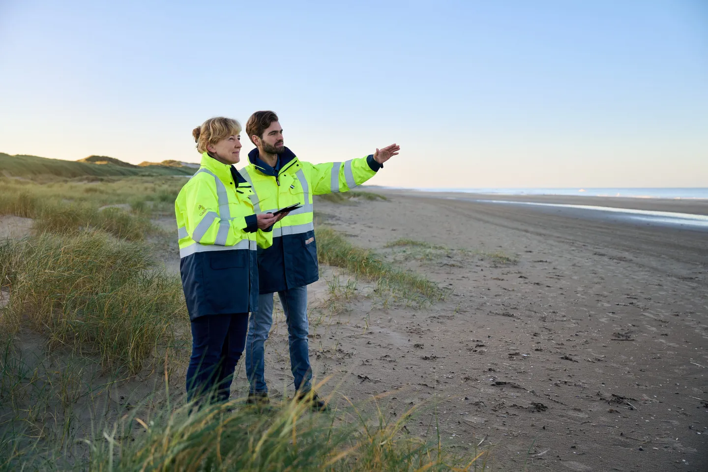 Twee Gasunie-medewerkers op het strand, met een tablet in de hand, die aanwijzingen geven naar de horizon.