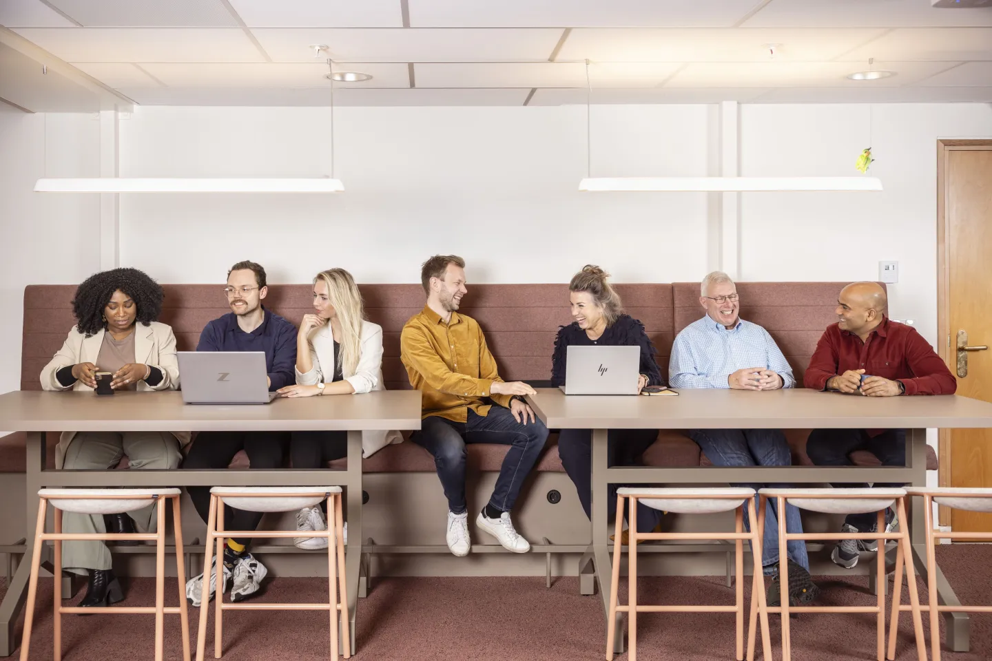 Mensen die aan een tafel zitten in een kantoorruimte, werken op laptops en communiceren met elkaar.