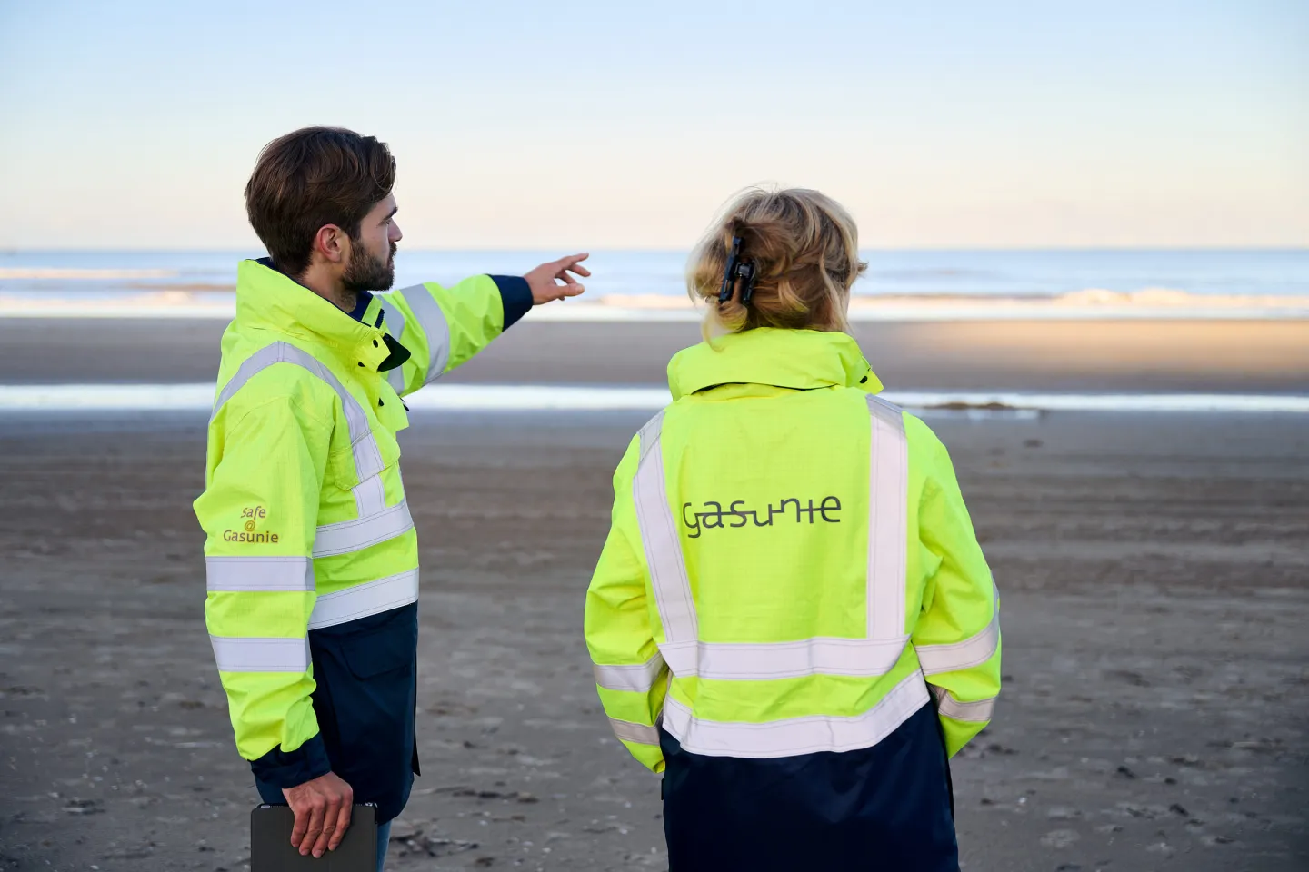 Gasunie-medewerkers op het strand, met de oceaan op de achtergrond, terwijl ze samenwerken aan een project.