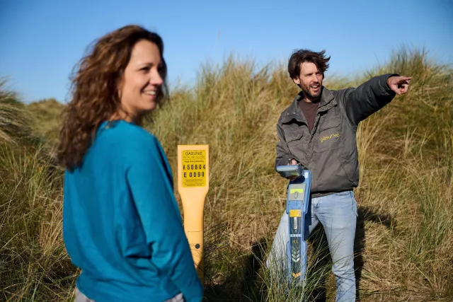 Gasunie-medewerkers die praten en wijzen naar de horizon op het strand, met zand en gras om hen heen.