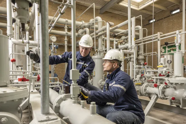 Twee technici die werken aan onderhoudswerkzaamheden terwijl ze pijpen en apparatuur afstellen.